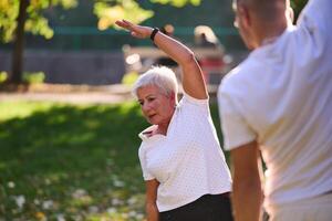 A group of seniors follows a trainer, engaging in outdoor exercises in the park, as they collectively strive to maintain vitality and well-being, embracing an active and health-conscious lifestyle in photo