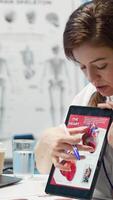 Vertical Woman specialist explaining heart function and condition on test results, doctor patient interaction in a cabinet. Physician cardiologist showing the cardiovascular system on tablet. Camera A. video