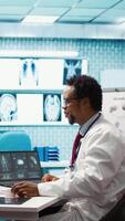 Vertical Expert evaluating diagnostic results with a patient in a medical cabinet, showcasing advanced healthcare technology using a screen displaying x rays and MRI scans. Care management. Camera B. video