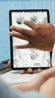 Vertical General practitioner pointing at the medical illustration to explain diagnosis to woman, discussing about x ray test analysis and looking at healthcare results. Checkup visit. Camera A. video