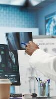 Vertical General practitioner examining x ray scan test results with patient, giving the right diagnostic report in medical cabinet. Doctor reviews analysis on health insurance, medical technology. Camera A. video