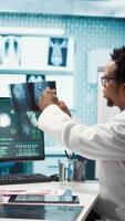 Vertical General practitioner examining x ray scan test results with patient, giving the right diagnostic report in medical cabinet. Doctor reviews analysis on health insurance, medical technology. Camera B. video