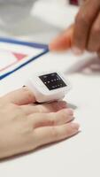 Vertical Physician using an oximeter on patient to measure oxygen levels and saturation, checking vital signs during examination at facility. Medic consulting a woman on health insurance. Close up. Camera A. video