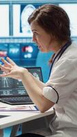 Vertical Female doctor and patient engage in a medical consultation with diagnostic tools and x ray imaging visible on the screen. Emphasizing modern healthcare practices and medical research. Camera A. video
