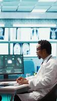 Vertical Male physician doing an x ray diagnostics scan interpretation during check up visit, discussing about recovery treatment in cabinet. Doctor examining radiography test results for a patient. Camera B. video