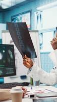 Vertical Medic expert showing the x ray imaging test results to patient at check up, discussing about treatment. Doctor pointing at radiography scans for interpretation, diagnostic report. Camera B. video
