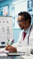 Vertical Doctor reading x ray imaging for a diagnostic report at consultation, discussing with a patient about medicine. Physician examining lab test results and analysis, health insurance. Camera B. video