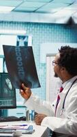 Vertical Physician reviewing MRI scan and x ray results with a patient in medical office, explaining the diagnostics. Doctor pointing at analysis to discuss about the illness, medical technology. Camera B. video