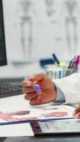 Vertical Professional medic analyzing x ray imaging and test findings in office, giving diagnostic report to patient at check up. African american specialist examines scans for interpretation. Camera A. video