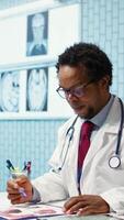 Vertical Professional medic analyzing x ray imaging and test findings in office, giving diagnostic report to patient at check up. African american specialist examines scans for interpretation. Camera B. video