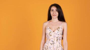 Beautiful brunette girl sky in front of the camera isolated on orange yellow background in studio video