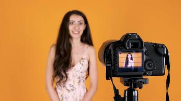 Beautiful girl vlogging in front of a camera with the focus to the camera on yellow orange background video