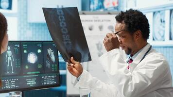 Medic expert showing the x ray imaging test results to patient at check up, discussing about treatment. Doctor pointing at radiography scans for interpretation, diagnostic report. Camera A. video