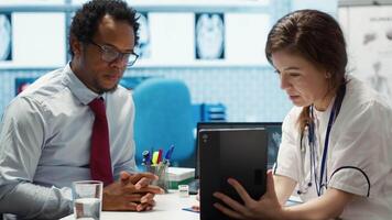 allmän praktiker presenter de testa resultat via skanna tolkning på läsplatta, diskuterar handla om de diagnostisk och möjlig behandling. medicinsk expert- tillhandahåller råd till patient. kamera a. video