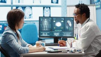 General practitioner presenting the diagnostic report at checkup with patient, discussing about treatment plan. Medic showing x ray imaging and scans on computer, medical results. Camera A. video