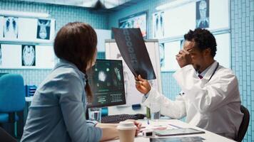 läkare expert- som visar de x stråle avbildning testa resultat till patient på kolla upp upp, diskuterar handla om behandling. läkare pekande på radiografi skannar för tolkning, diagnostisk Rapportera. kamera b. video