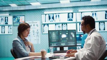 Doctor reading x ray imaging for a diagnostic report at consultation, discussing with a patient about medicine. Physician examining lab test results and analysis, health insurance. Camera B. video