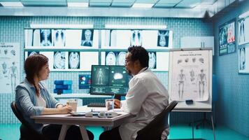General practitioner presenting the diagnostic report at checkup with patient, discussing about treatment plan. Medic showing x ray imaging and scans on computer, medical results. Camera B. video