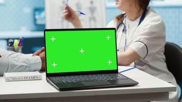General practitioner and patient looking at green screen on device, recommending pills and drugs during check up visit. Diverse people discussing about diagnostics and remedy. Camera A. video