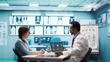 esperto valutare diagnostico risultati con un' paziente nel un' medico mobiletto, in mostra Avanzate assistenza sanitaria tecnologia utilizzando un' schermo visualizzazione X raggi e mri scansioni. cura gestione. telecamera b. video