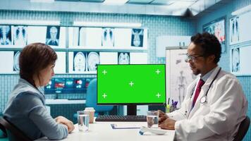 General practitioner consulting a female patient next to isolated chroma key display, sharing insight on lab test results and analysis. Skilled medic supports his client, indoors check up. Camera B. video