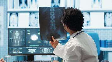Physician reviewing MRI scan and x ray results with a patient in medical office, explaining the diagnostics. Doctor pointing at analysis to discuss about the illness, medical technology. Camera A. video