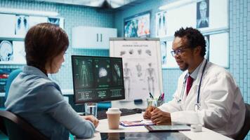Doctor reading x ray imaging for a diagnostic report at consultation, discussing with a patient about medicine. Physician examining lab test results and analysis, health insurance. Camera B. video
