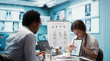 Healthcare provider presenting lab test results to a patient in cabinet, reviewing x ray and MRI scans to assist man through recovery. Medical technology in diagnostics and care management. Camera B. video