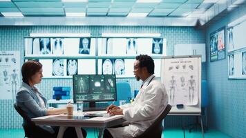Male physician doing an x ray diagnostics scan interpretation during check up visit, discussing about recovery treatment in cabinet. Doctor examining radiography test results for a patient. Camera B. video