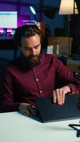 Vertical Tech expert assessing laptop performance, talking about components used inside, filming with smartphone. Entertainer reviewing notebook on technology internet channel, recording with phone, camera B video