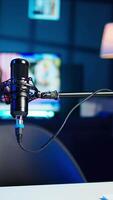 Vertical Close up shot of professional streaming microphone in empty neon lit studio used for online content production. Panning shot of content creation recording mic in apartment video