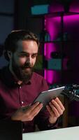 Vertical Tech specialist presenting tablet in entry level low budget price range to interested viewers, filming with smartphone on tripod. Man reviewing digital device, recording with mobile phone, camera B video