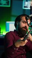 Vertical Influencer doing peace sign in front on cellphone attached to selfie stick in studio, chatting with viewers using mic. Man doing hand gesturing, using phone and microphone to record vlog, camera A video