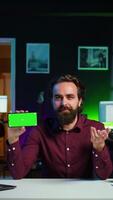 Vertical Man showing green screen cellphone, using it as empty copy space to showcase his online streaming channel logo. Media star does introductory using chroma key phone, camera B video