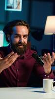 Vertical Joyful media star talking in professional microphone in studio at night, filming internet production. Smiling content creator uses quality mic to record vlog and speak to viewers, camera A video