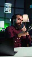 Vertical Influencer doing peace sign in front on cellphone attached to selfie stick in studio, chatting with viewers using mic. Man doing hand gesturing, using phone and microphone to record vlog, camera B video