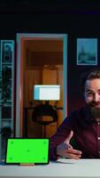 Vertical Tech engineer presenting green screen tablet in low budget price range, filming from dimly lit home studio. Content creator reviewing mockup digital device in front of online audience, camera B video