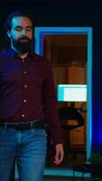 Vertical Content creator adjusting professional microphone in studio before starting vlog, recording with selfie camera. Man in neon lit home studio preparing equipment, filming with smartphone, camera B video