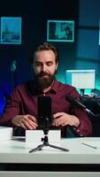 Vertical Media star in neon lit studio presents cellphone from brand sponsoring , analyzing features. Influencer reviews phone for technology enthusiasts following his social media account, camera B video