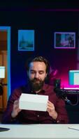 Vertical Content creator receiving mystery box from subscribers, ready to film packaged product unboxing. Internet star pointing to surprise package received, recording in home studio, camera B video