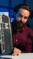 Vertical Influencer in studio reviewing gaming keyboard, mouse and headphones. Online show host filming electronics haul, presenting wired computer peripherals to viewers during live broadcast, camera A video