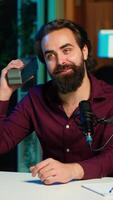 Vertical Smiling media star doing technology review of wireless portable speaker for online platforms channel. Cheerful influencer presenting music playing device to his audience, camera A video