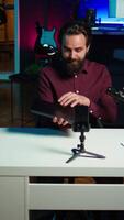 Vertical Man in studio endorsing laptop from brand sponsoring , filming with smartphone on tripod. Tech expert does influencer marketing by promoting notebook, recording with phone, camera B video