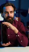 Vertical Entertaining man in studio films tablet review for tech enthusiasts. Viral media star hosts technology internet show, unboxing digital portable device, feeling impressed by thinness, camera A video