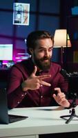 vertical influenciador fala dentro frente em Smartphone em anexo para tripé e Alto qualidade microfone dentro estúdio, discutindo com espectadores. homem usando Móvel telefone e profissional engrenagem para registro social meios de comunicação , Câmera b video