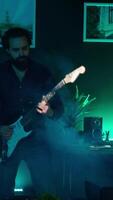 Vertical Playful internet star playing guitar in studio while shooting . Energetic content creator playing musical instrument while filming vlog with professional mic in home studio, camera A video