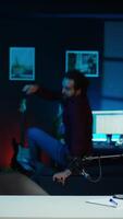 Vertical Playful online star using tech equipment to shoot , doing frantic gesturing. Energetic content creator jumping on chair, having fun while filming vlog with professional mic in studio, camera B video