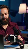 Vertical Tech vlogger reviewing VR goggles in neon lit studio. Entertaining content creator filming technology channel vlog for gadget enthusiasts using professional camera and mic, camera A video