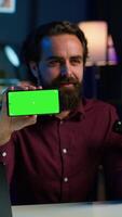 Vertical Man showing green screen cellphone, using it as empty copy space to showcase his online streaming channel logo. Media star does introductory using chroma key phone, camera A video