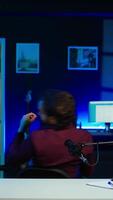 Vertical Childish man doing creative intro for vlog, using microphone to shoot . Energetic content creator spinning on chair while filming for vlogging channel with mic in home studio, camera B video
